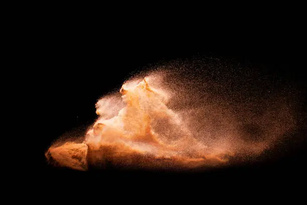 Photo of Sand explosion isolated on black background. Freeze motion of sandy dust splash.