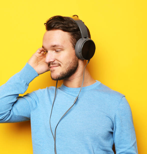 istock Young stylish man adjusting his headphones and smiling while standing against yellow background 1325673620