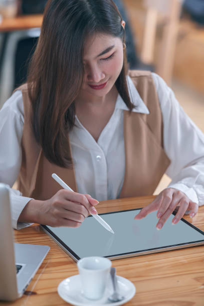 istock Young asian woman using stylus pen writing on tablet screen while sitting at her desk in office. 1325678071