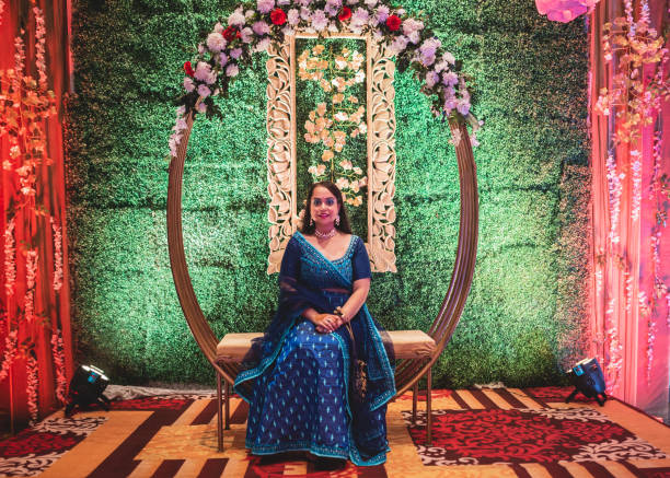 novia india en vestido azul lehenga sentado en un asiento decorado con flores en una etapa de la boda con una hermosa decoración simple. - women bride personal accessory adult fotografías e imágenes de stock