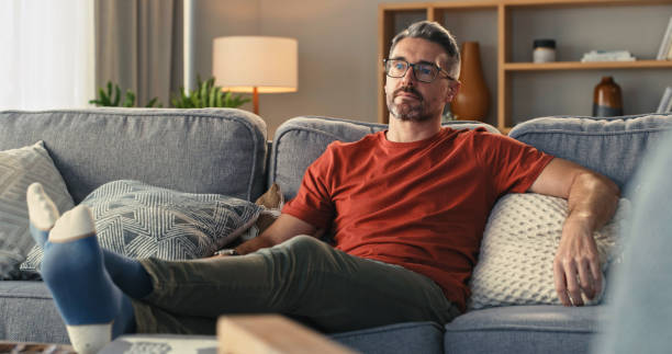 plan d’un homme mature se relaxant sur le canapé à la maison - regarder la télévision photos et images de collection