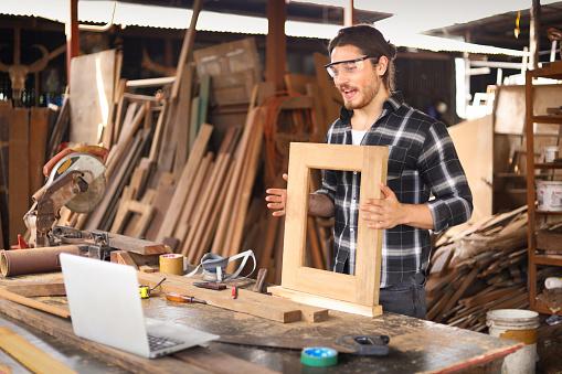 Caucasian carpenter is describing his wooden frame product to the online bidding customer in live streaming via internet marketing for his small business art products