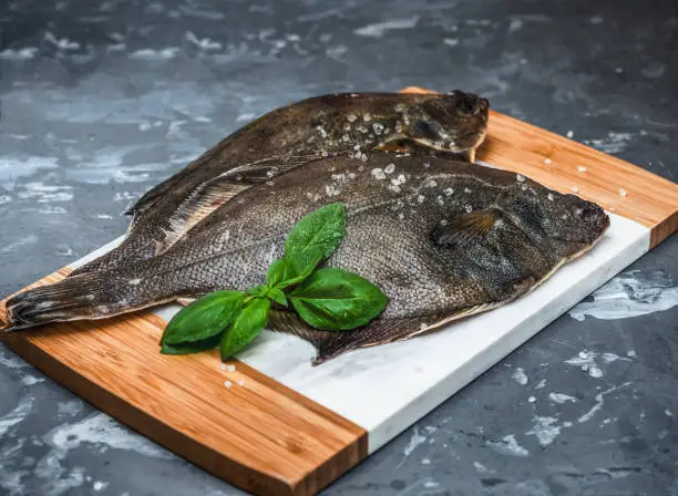Raw fish flounder with salt and basil on a kitchen board close-up