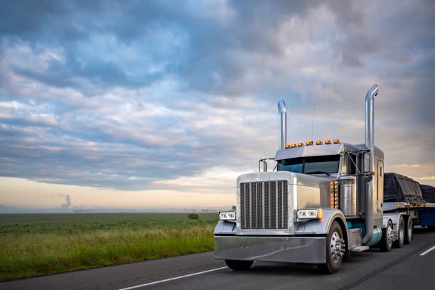 beautiful classic big rig american semi truck with light transporting covered cargo on flat bed semi trailer driving on the twilight highway road with stormy clouds sky - 鉸接式貨車 個照片及圖片檔