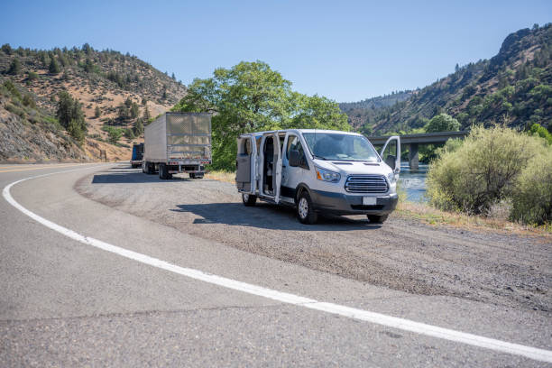 istock Compact mini van and big rig semi trucks with semi trailers take a break standing on the road shoulder on the bank of a mountain river 1325693343