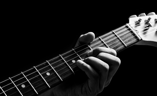 close up male musician left hand playing chord on electric guitar neck. music background
