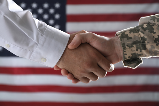 Soldado y hombre de negocios estrechando la mano contra la bandera de EE.UU., primer plano photo