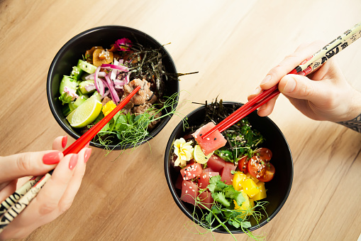 Man and woman eating poke salad with chopsticks. Dab tuna salad in a bowl. People in the restaurant eat salad with chopsticks. Asian seafood salad concept