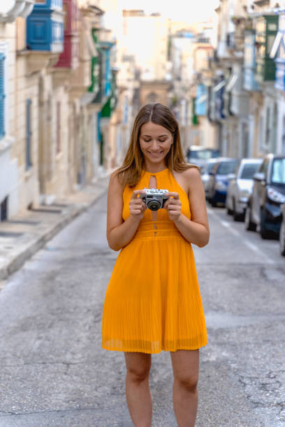 Portrait of a beautiful woman in a traditional Sliema alley. Malta young woman with a retro camera and yellow dress in Malta valletta photos stock pictures, royalty-free photos & images