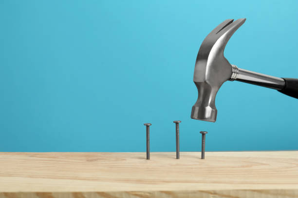 istock Hammering nail into wooden surface against light blue background, space for text 1325699589