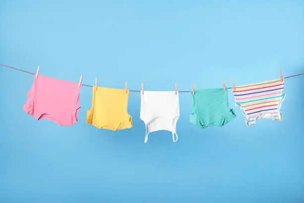 Clean child's clothes hanging on laundry line against light blue background