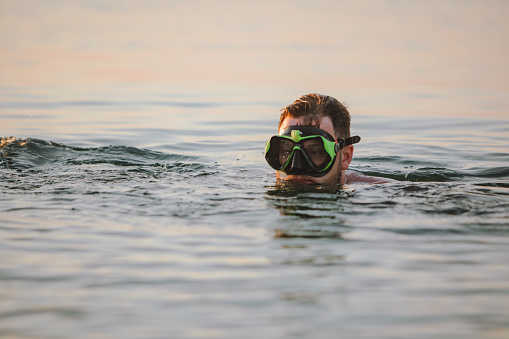 man with snorkeling mask in water on sunset close up