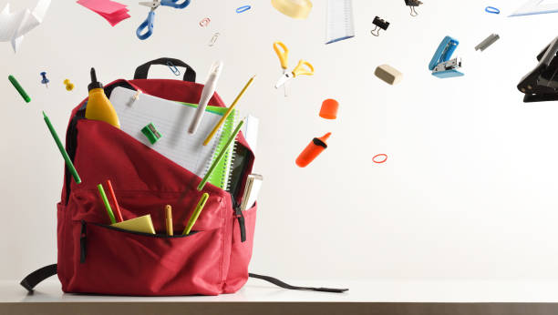 School supplies flying and coming out of school backpack Study desk and school supplies flying coming out of a school backpack with white isolated background.. Front view. Horizontal composition. stapled paper stock pictures, royalty-free photos & images