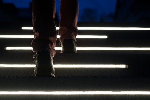 Male legs in boots climb the illuminated stone steps on a winter night. Close-up. Bottom view.