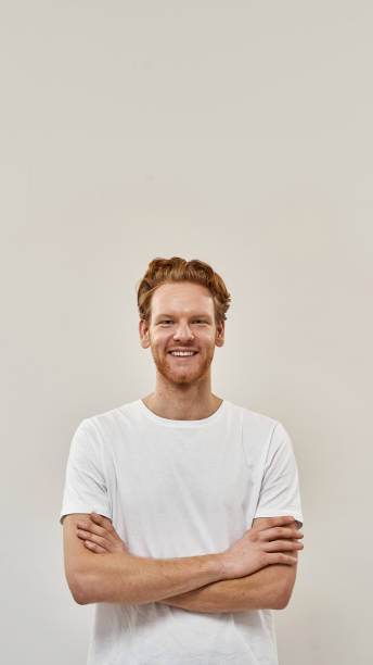 un jeune homme rousse se tient les bras croisés et regarde droit à huis clos - t shirt white men jeans photos et images de collection