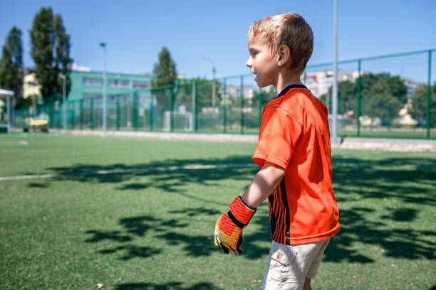 kleiner junge in schwarz und orange fußballform fußball spielen fußball auf offenem feld in hof, junge torhüter - playing field goalie soccer player little boys stock-fotos und bilder