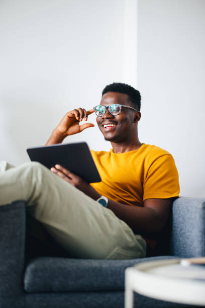 praca z domu: uśmiechnięty młody afroamerykanin za pomocą tabletu - men shirt people black zdjęcia i obrazy z banku zdjęć