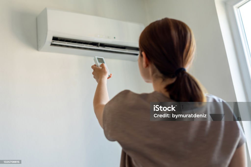 Woman turning on air conditioner with remote Air Conditioner Stock Photo