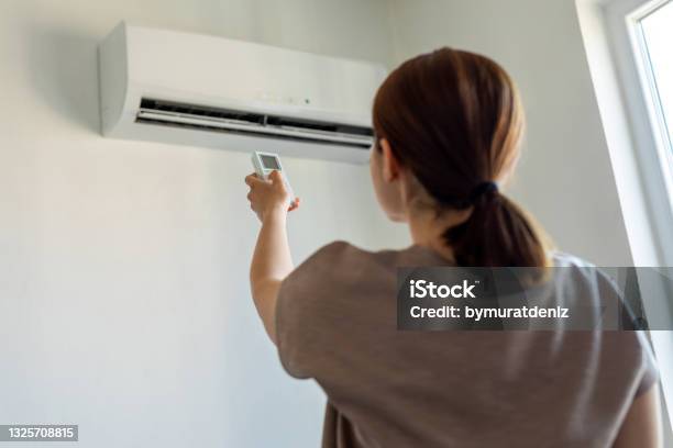 Woman Turning On Air Conditioner With Remote Stock Photo - Download Image Now - Air Conditioner, Domestic Life, Home Interior