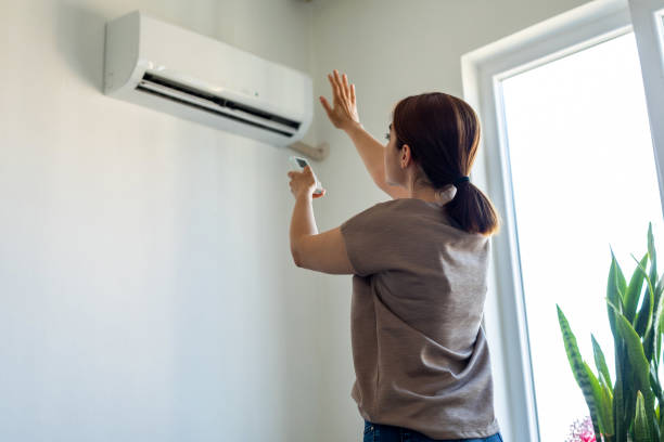 Woman turning on air conditioner Woman turning on air conditioner adjusting stock pictures, royalty-free photos & images
