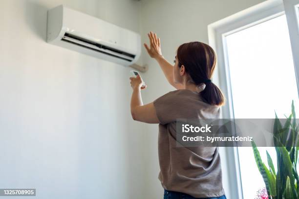Woman Turning On Air Conditioner Stock Photo - Download Image Now - Air Conditioner, Domestic Life, Residential Building