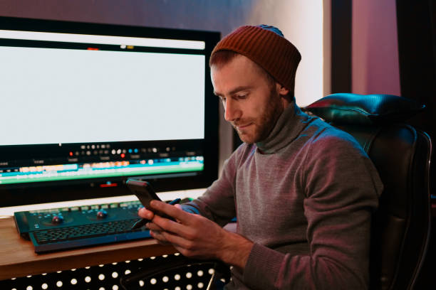 istock Male Video Editor sitting at his Computer using phone 1325709152