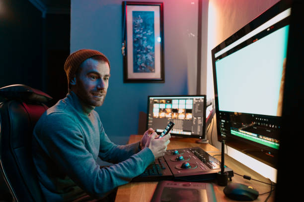 istock Male Video Editor sitting at his Computer using phone blank screen 1325709274