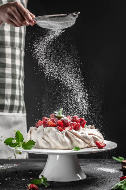 delicious homemade Pavlova cake with fresh strawberries and whipped cream. chef hands with powder in a freeze motion of a cloud of powder midair. Culinary, cooking, bakery concept delicious homemade Pavlova cake with fresh strawberries and whipped cream. chef hands with powder in a freeze motion of a cloud of powder midair. Culinary, cooking, bakery concept, pavlova stock pictures, royalty-free photos & images