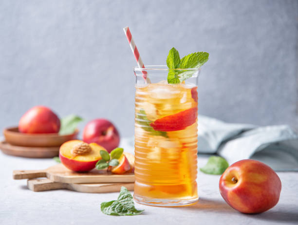 cool peach tea with mint and ice in a glass on a blue background. front view and copy space - chá gelado imagens e fotografias de stock