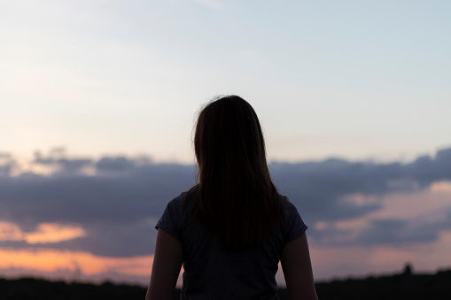 Young lonely woman looks at the sunset. utdoor photo. Dark silhouette.