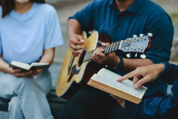 las familias cristianas adoran a dios en el jardín tocando la guitarra y sosteniendo una santa biblia. agrupa a las personas cristianas que leen la biblia juntas. concepto de sabiduría, religión, lectura, imaginación. - small group of people fotografías e imágenes de stock