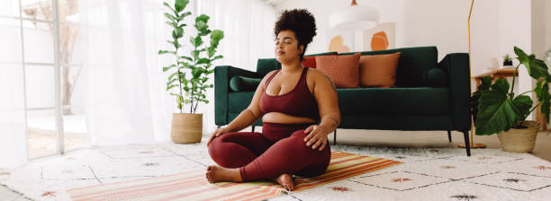 femme positive pour le corps en train de faire de la méditation à la maison - floor women sitting yoga photos et images de collection