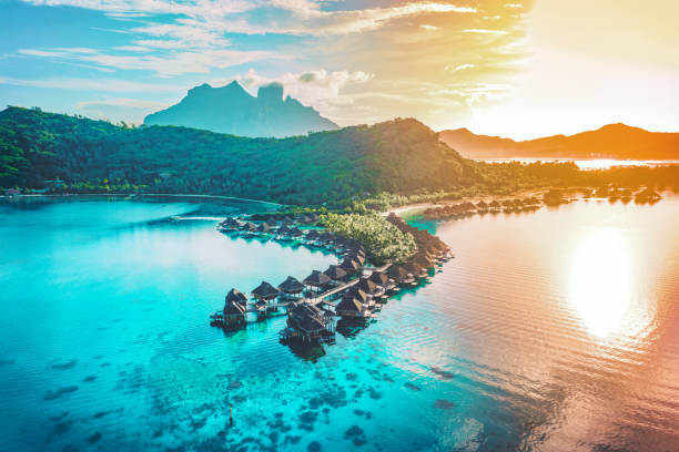 luxury travel vacation aerial of overwater bungalows resort in coral reef lagoon ocean by beach. view from above at sunset of paradise getaway bora bora, french polynesia, tahiti, south pacific ocean - empreendimento turístico imagens e fotografias de stock