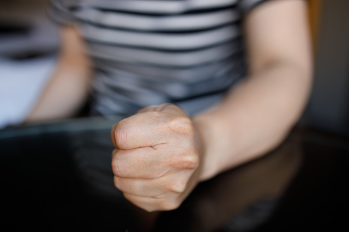 Close-up of a woman’s fist banging on a wooden table.