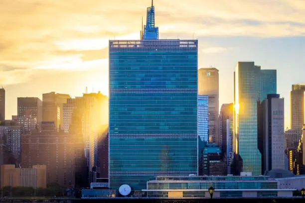 The sun peeks out from behind the UN building as it begins to set, creating golden rays across the NYC skyline.