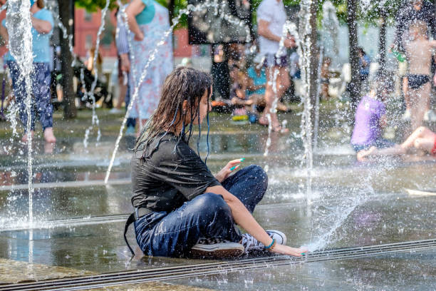 młoda dziewczyna w mokrych ubraniach siedzi na podłodze fontanny ulicznej - sprinkler park summer spray zdjęcia i obrazy z banku zdjęć