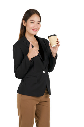 Young asian women in black suit with a smile lifted a finger thumb up while holding a cup of coffee. Portrait on white background with studio light.