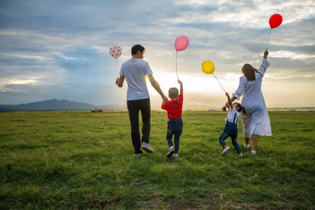 Photo of soft focus of Asian family holding the balloon and walking on the Meadow at sunset with happy emotion. Family Holiday and Travel concept.