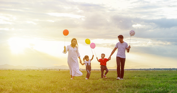 soft focus of Asian family holding the balloon and walking on the Meadow at sunset with happy emotion. Family Holiday and Travel concept.