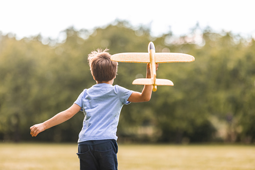 Rear view of little boy playing with airplane toy outdoors