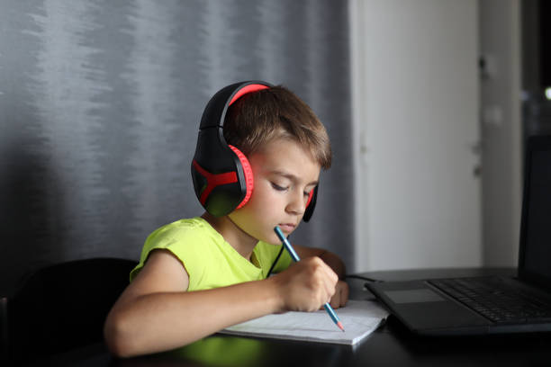 istock Boy with headset listening to lesson and writing in notepad at home 1325755108