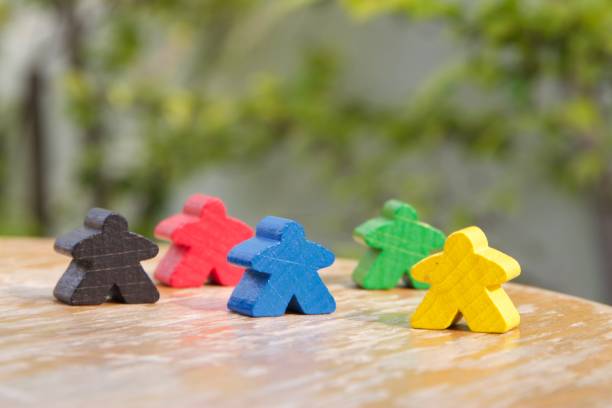 meeples colorés, jaune, noir, rouge bleu et vert, sur une chaise ronde en bois sous le concept de diversité et de vivre paisiblement entre différentes ethnies, horizontale - meeple photos et images de collection