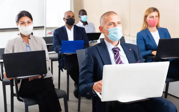 Group of multinational people in protective masks working on laptops during a business seminar