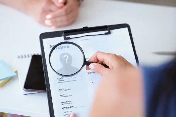 Photo of Employer looking at worker resume with magnifying glass closeup