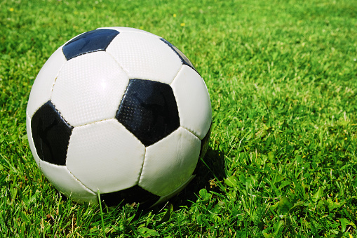 Classic soccer ball on bright green grass on the football field. Summer playing sports. Copy space.