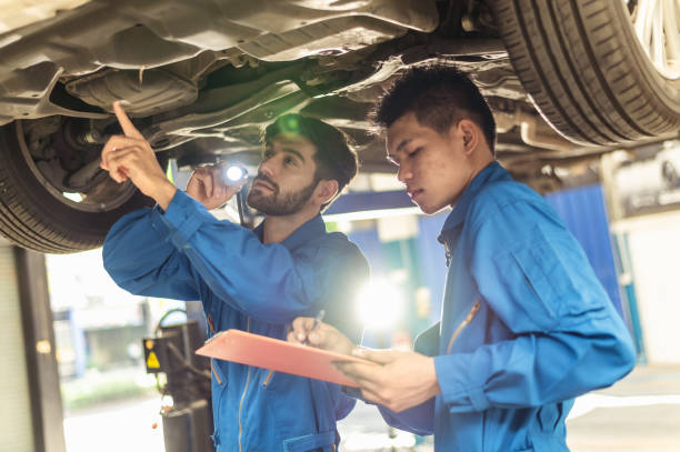 istock Two professional look technician inspecting car underbody and suspension system by using check list in modern car service shop. Automotive business or car repair concept. 1325772307