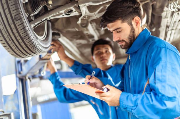 Two professional look technician inspecting car underbody and suspension system by using check list in modern car service shop. Automotive business or car repair concept. Two professional look technician inspecting car underbody and suspension system by using check list in modern car service shop. Automotive business or car repair concept. automobile industry stock pictures, royalty-free photos & images