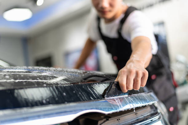 technik pracownik owijania kaptur pojazdu za pomocą ochraniacza winylu folii do ochrony malarstwa samochodowego od podstaw. - protective varnish zdjęcia i obrazy z banku zdjęć