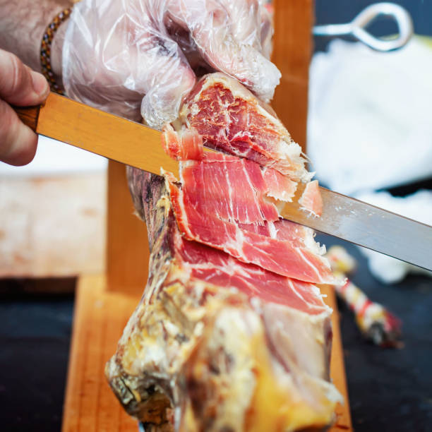 istock Butcher cuts jamon with knife. Spanish ham, Jamon Serrano, Italian Prosciutto, selective focus 1325777362
