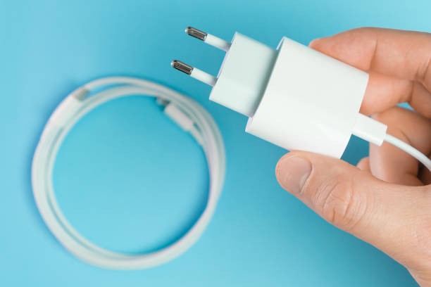 A white smart phone charger cable with lightning hi speed USB type C connector and adapter in man hand on the blue background.